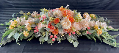 Four foot long casket spray made up of peach, apricot , and dusty pink  assorted flowers accented by sage eucalyptus.