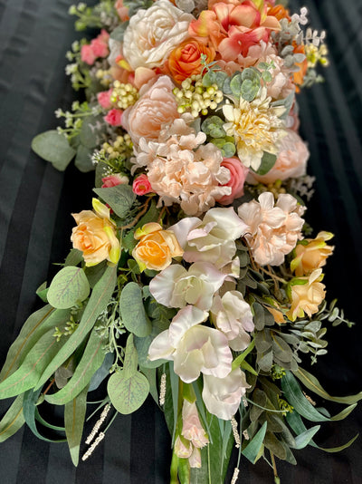 Four foot long casket spray made up of peach, apricot , and dusty pink  assorted flowers accented by sage eucalyptus.