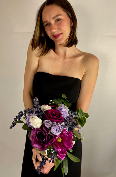 This vibrant jewel toned bridesmaid bouquet features a gradient of rich violet and fuchsia roses, white chrysanthemum, pale purple dahlia, amethyst hydrangea, thistle, lavender, and green succulent sprigs.This bouquet rents for $59.00 for five days.