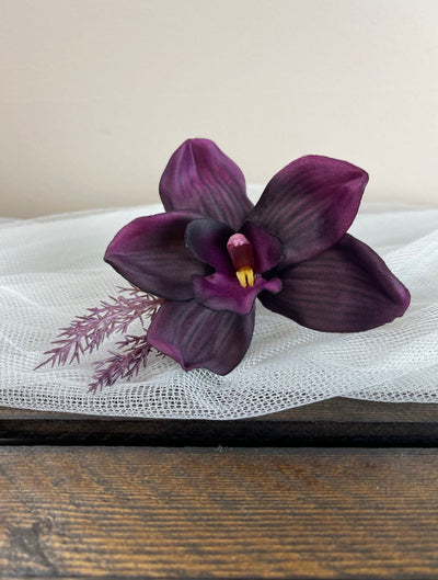 Boutonniere from our Black Cherry Collection. Crafted with a single deep, rich eggplant orchid and two sprigs of wild wispy lavender, it is artfully wrapped in a luxuriant deep plum satin.
