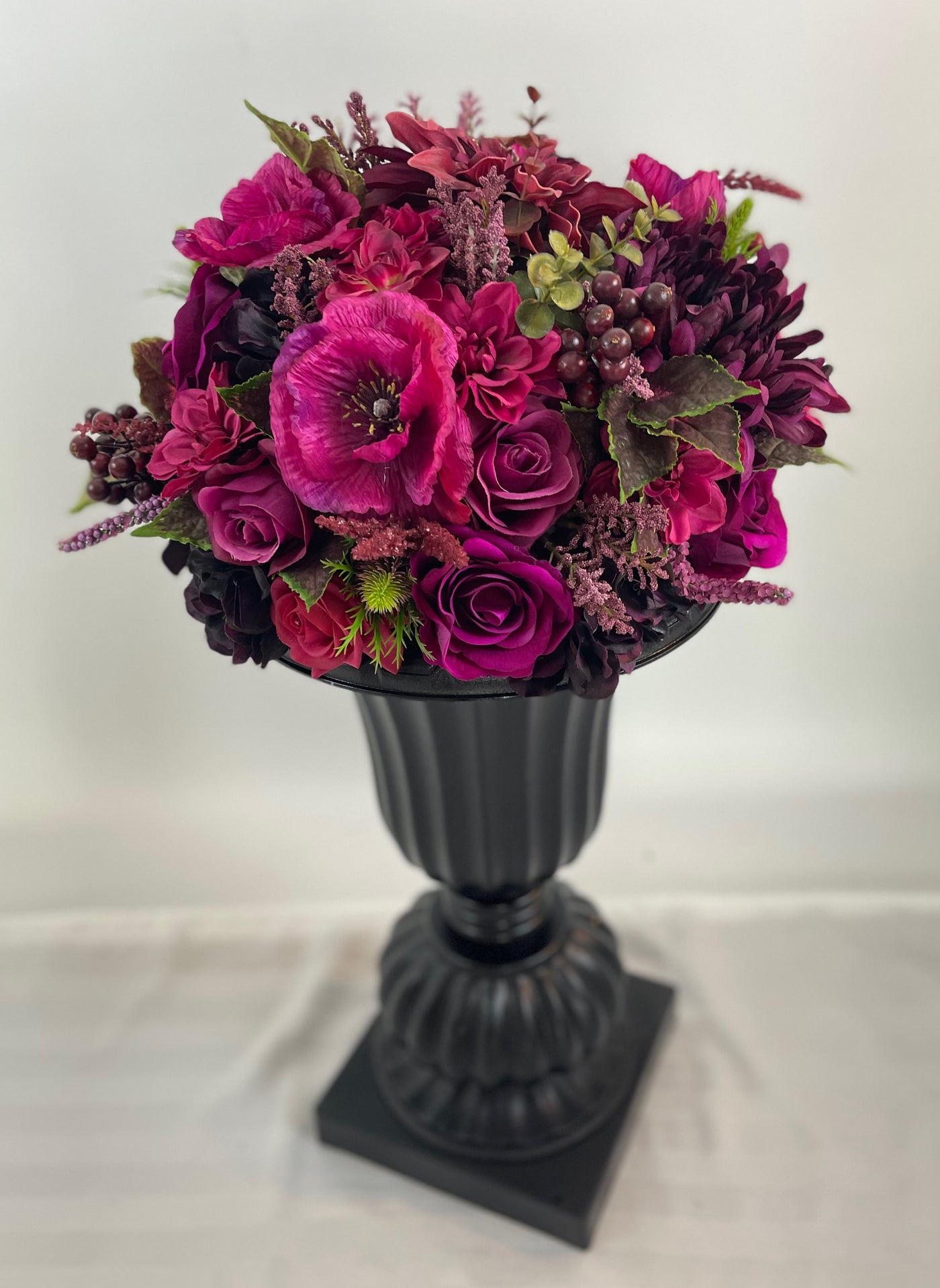 Elevating any space with its height of 2 feet 4 inches, this sophisticated black planter boasts an abundance of opulent magenta blossoms. 