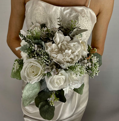 This one-of-a-kind bridesmaid bouquet is a stunning combination of timeless elegance and natural beauty. Its soft white roses, hydrangea, and dahlias pair perfectly with three shades of sage eucalyptus and a touch of dusty miller — all wrapped up in a delicate white satin ribbon and tulle for a look of sophistication on your special day!