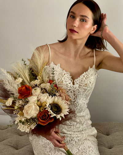 This side held bridal bouquet combines ivory, cappuccino, and rust roses, with cream sunflowers, mini dahlia, pampas, feathers, wheat grass, thistle and sage eucalyptus to create a  relaxed natural bohemian vib