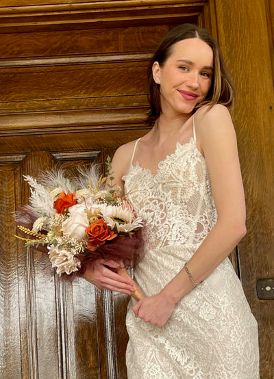 This side held bridal bouquet combines ivory, cappuccino, and rust roses, with cream sunflowers, mini dahlia, pampas, feathers, wheat grass, thistle and sage eucalyptus to create a  relaxed natural bohemian vib