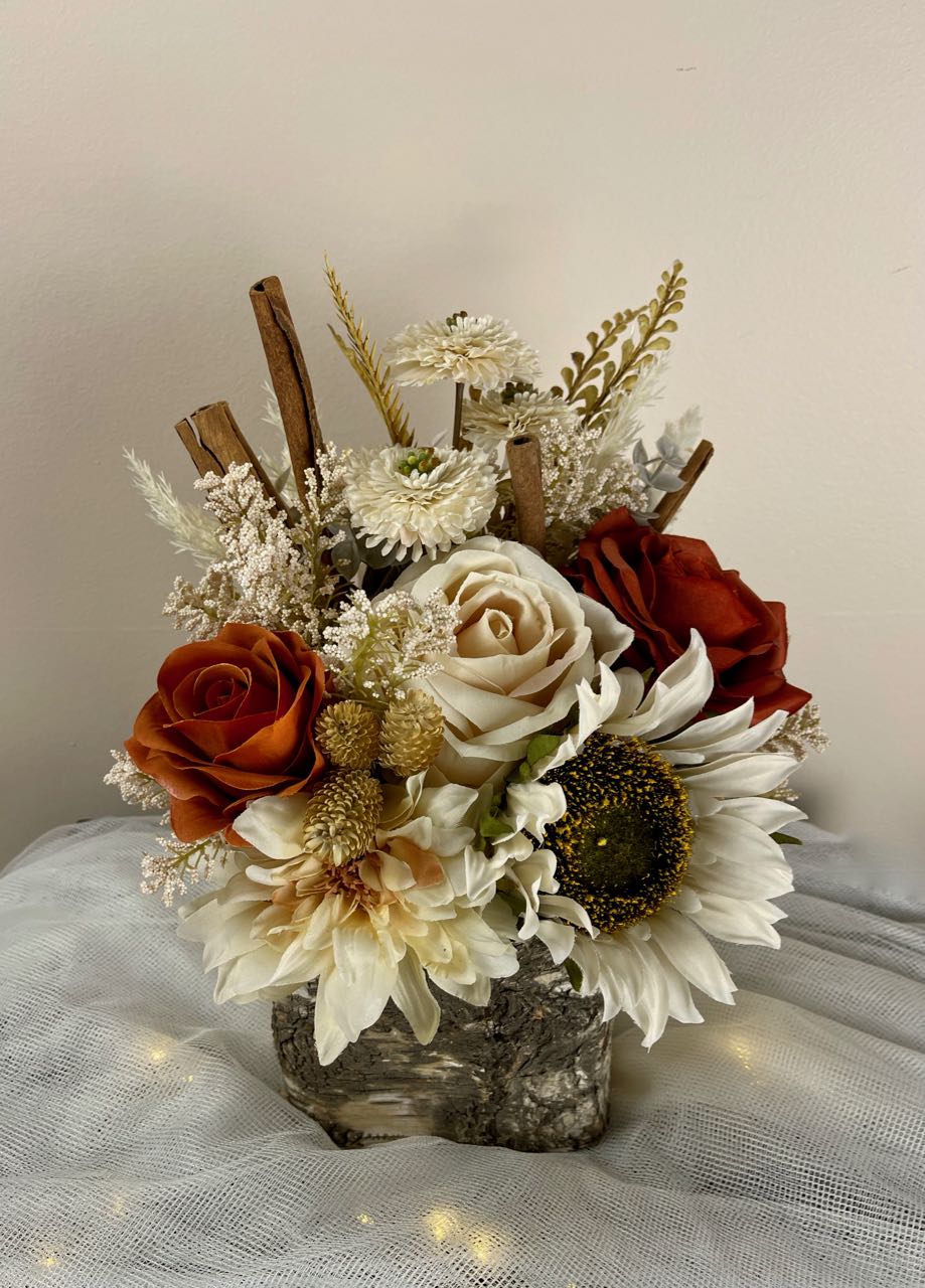Rent A Rose This centrepiece features rust and cream roses combined with pampas, eucalyptus, and for a fun twist, cinnamon sticks, all nestled in a birch vase. The centrepiece is approx. 8 inches wide by 12 inches tall. 
