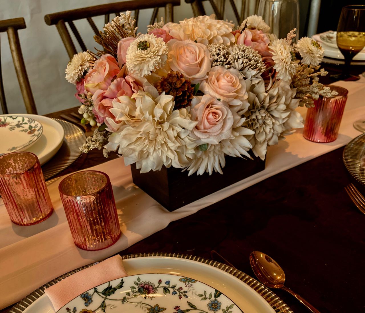This soft-toned cream, blush and rich brown centrepiece features earth elements such as pine cones and chocolate brown pincushions. This earthy heartiness is juxtaposed with the delicate petals of large pompom dahlias, cream sunflowers, blush floribunda roses, champagne hydrangeas, and accented with cream snowberries.  This Bohemian inspired creation is enveloped by muted grey-green seeded eucalyptus and finally finished in an espresso stained wood box (L8”x W4”x H