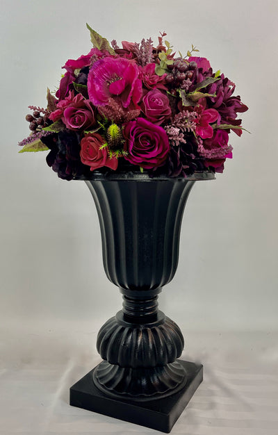 Elevating any space with its height of 2 feet 4 inches, this sophisticated black planter boasts an abundance of opulent magenta blossoms. 