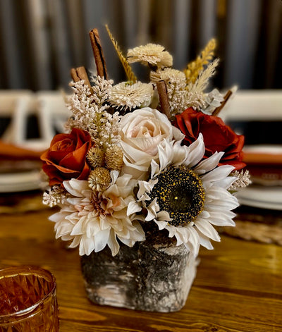 This centrepiece features rust and cream roses combined with pampas, eucalyptus, and for a fun twist, cinnamon sticks, all nestled in a birch vase. The centrepiece is approx 8 inches wide by 12 inches tall. This earthy concoction would not look out of place on a cocktail table,  however it has enough presence and height to be used on a 8 foot round tale surrounded by candle votives.
