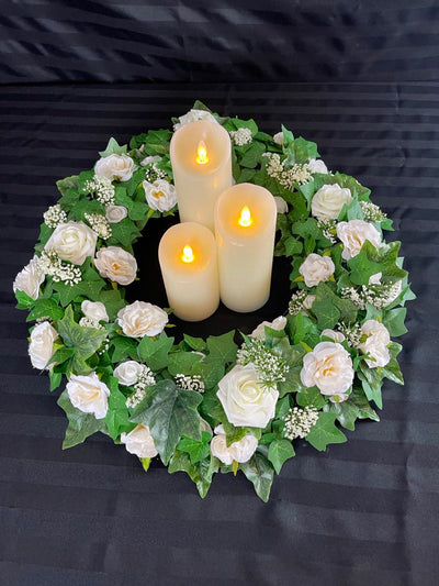 Dark green ivy with various sizes of white roses interspersed between the leaves create this simple yet elegant centrepiece. The ring can be used alone but we love the look of adding in cream pillar candles. Select the number of LED pillar candles you would like to complete this look. The outer circumference of this wreath is 21 inches and in inner circumference is 10 inches. Pillar candles to be rented separately. Each pillar candle is an additional $3.00 to $4.00 to rent.
