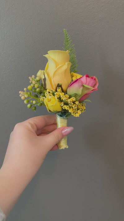 This 6" yellow boutonniere features yellow and pink roses, and delicate foliage, secured with a yellow or pink satin ribbon.