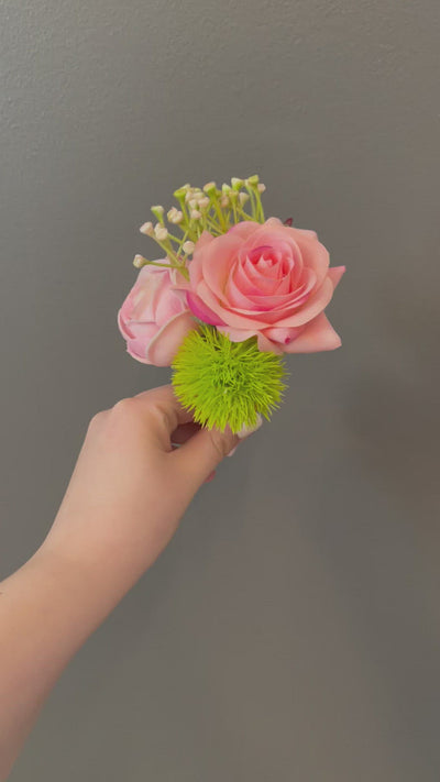 A green grass ball and a lovely spring of greenery offer a playful accent to a pale pink cabbage rose and a rich pink tea rose. This design could easily be recreated in icing on beautiful cupcakes. Delightfully fun!