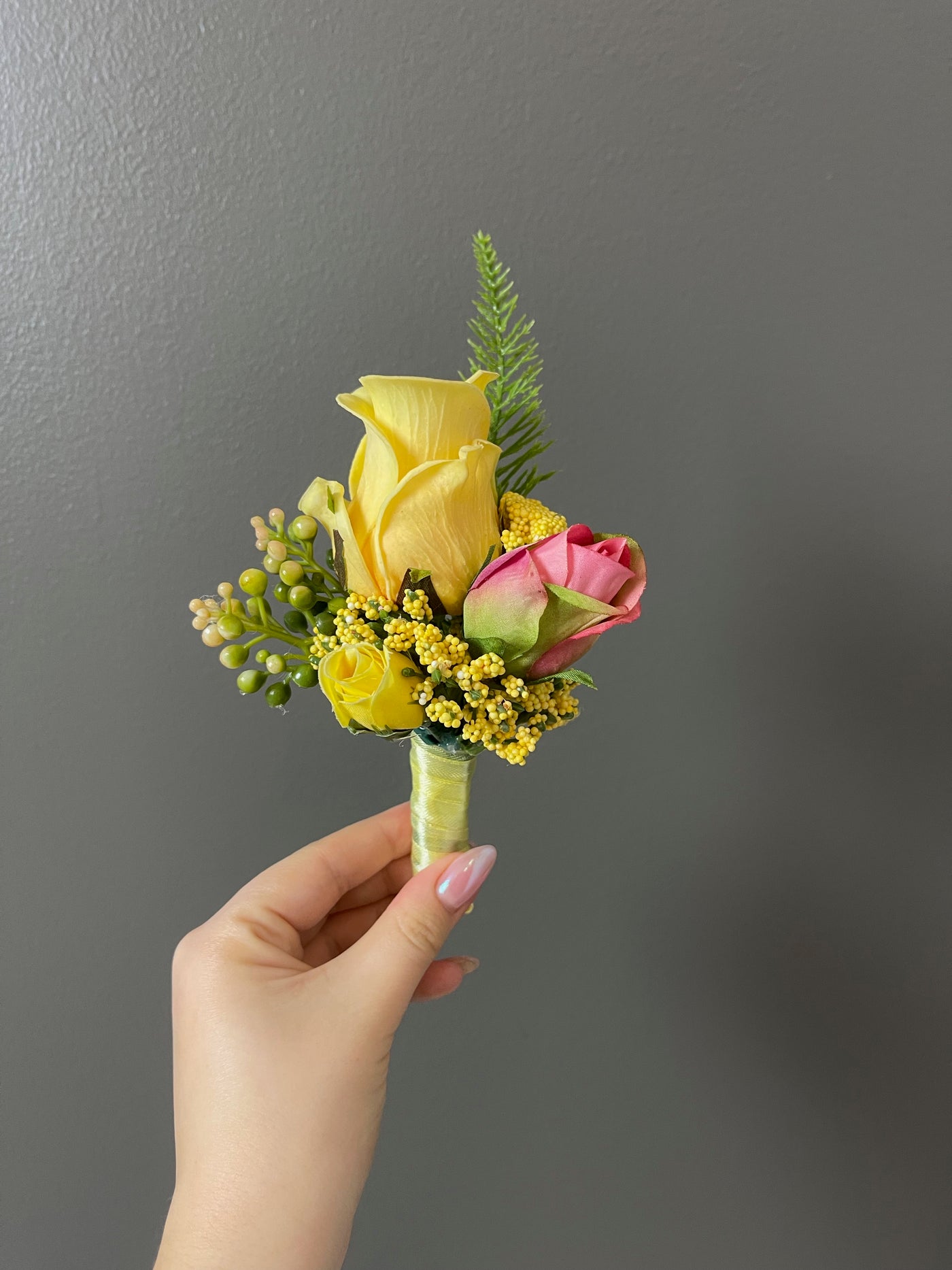 This 6" yellow boutonniere features yellow and pink roses, and delicate foliage, secured with a yellow satin ribbon.