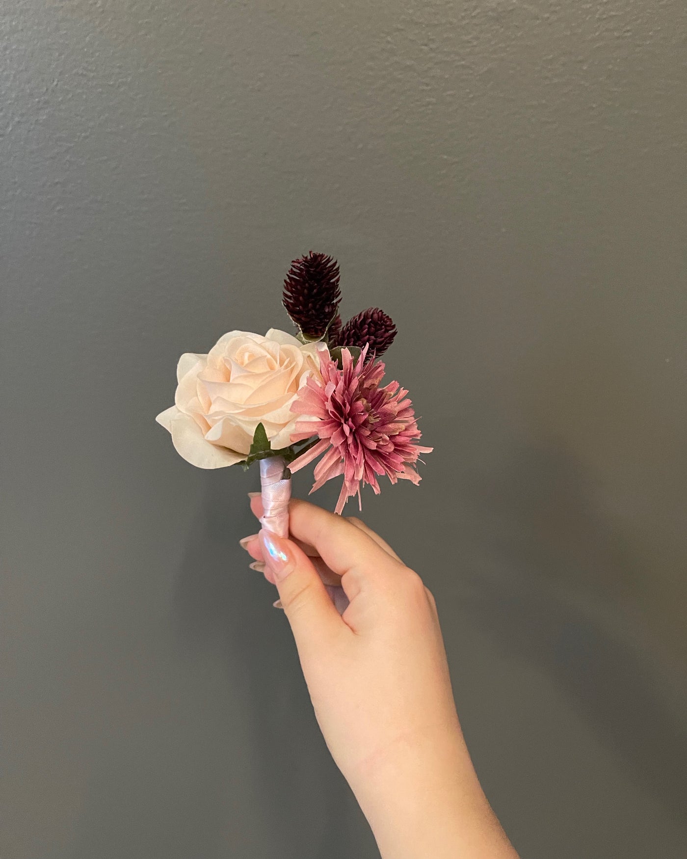 This 6" boutonniere features a pale pink rose, a spider mom, burgundy thistle, and finished with a satin pink ribbon.