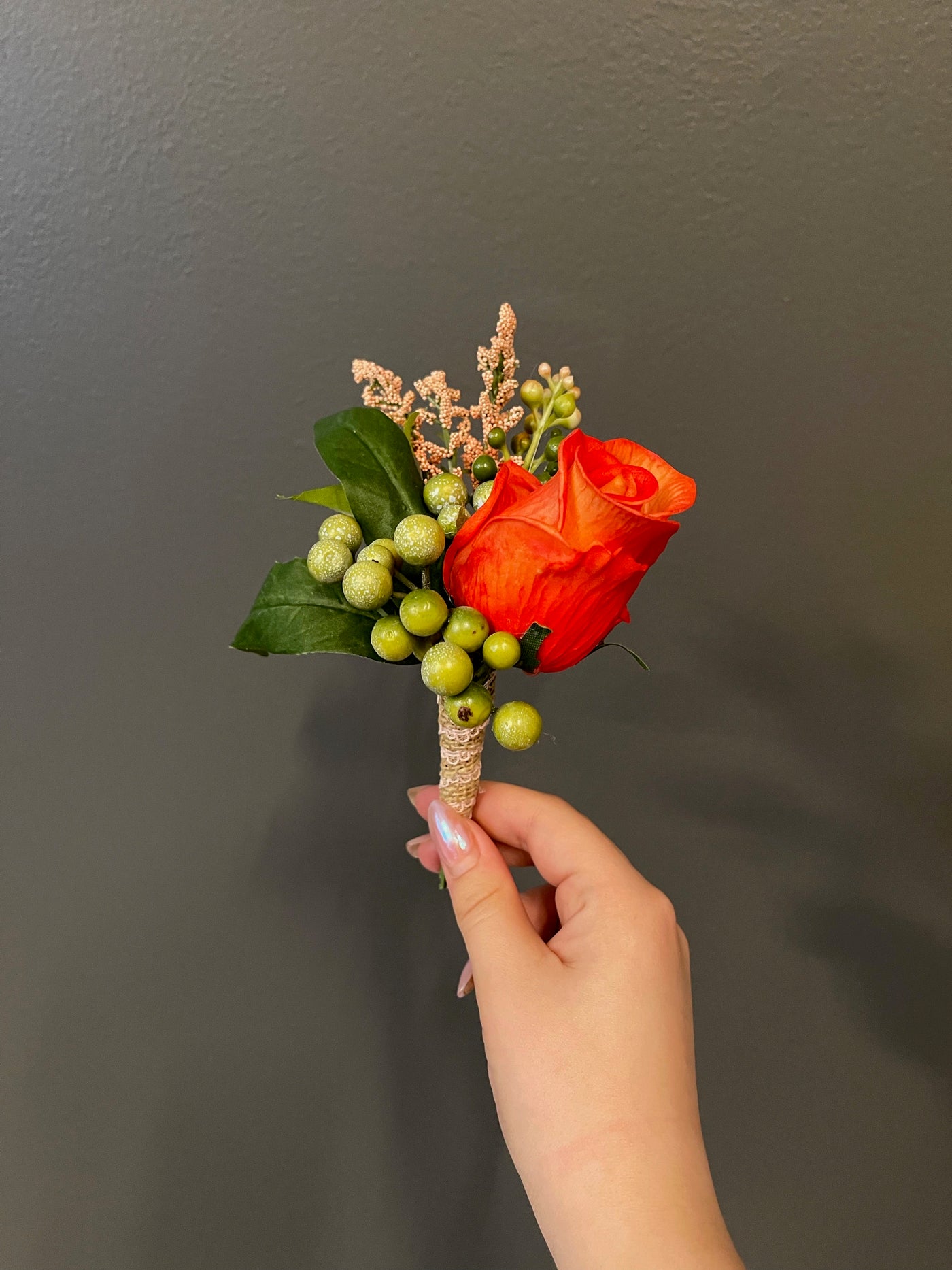 A single dramatic orange rose coupled with green hypericum berries and peach tree leaves wrapped in a burlap ribbon.A single dramatic orange rose coupled with green hypericum berries and peach tree leaves wrapped in a burlap ribbon.