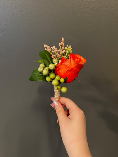 A single dramatic orange rose coupled with green hypericum berries and peach tree leaves wrapped in a burlap ribbon.A single dramatic orange rose coupled with green hypericum berries and peach tree leaves wrapped in a burlap ribbon.