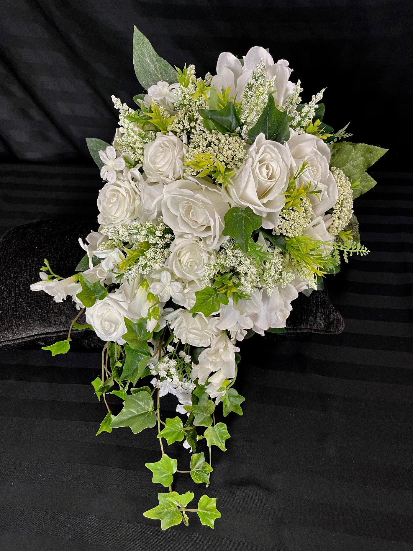 Savour the elegant lines of this cascading all white bridal bouquet. This lovely compilation of three different sizes of crisp white roses nestled in deep green Ivy foliage with playful astilbe peeking out is the epitome of elega