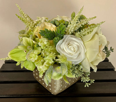 Roses in cream, ivory and white are combined effortlessly with green hydrangea, orchids and astilbe. This exquisite arrangement is accented by olive hypericum berries&nbsp;and thistle to create a perfect centrepiece for a high top cocktail table. This lovely arrangement is 5 inch x 5 inch and sits in a concrete vase accented at the bottom with gold foil.