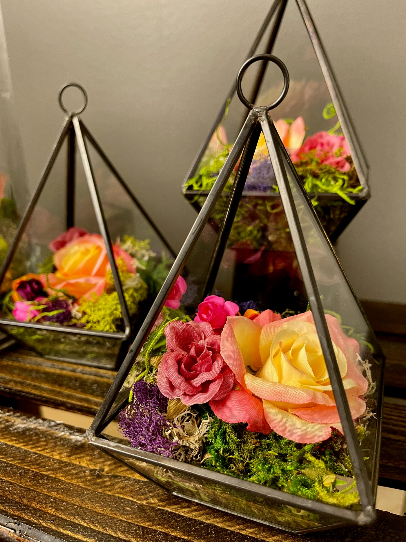 Three glass pyramids with Black Iron  details holding multi coloured moss and mini rosebud heads.