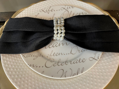 Black napkin made into a bow tie shape by a three string pearl napkin ring holder.