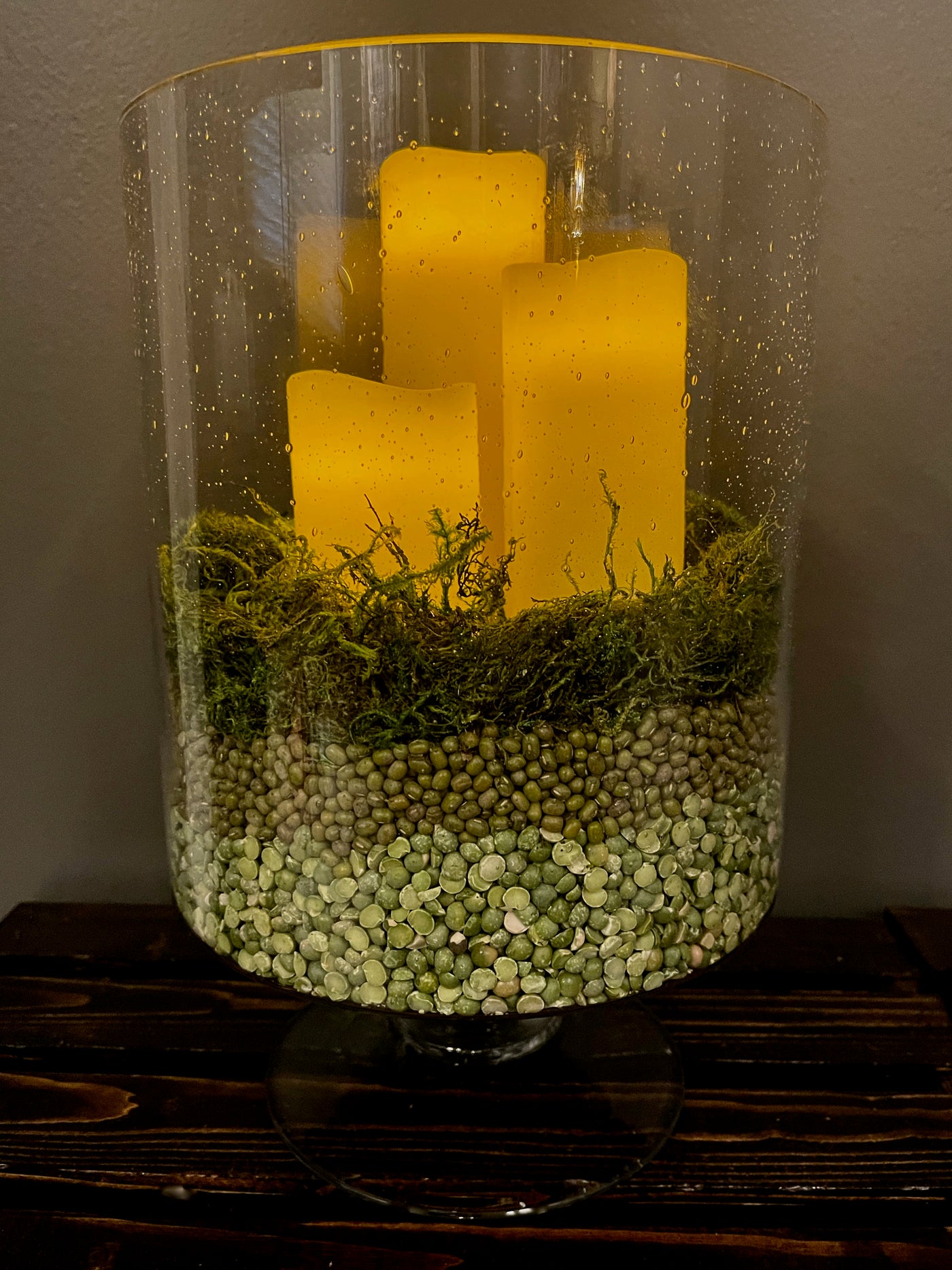 Set of three thick glass 12" pedestal vases, each holding three remote controlled LED Ivory candles nestled in a deep rich moss base