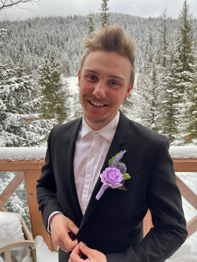 Rent A Rose-This 6" boutonniere features a light purple rose, sprigs of lavender, thistle, eggplant rose, and evergreen foliage detail, finished with a light purple ribbon.