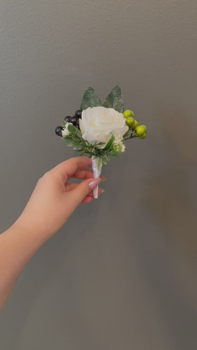 This 6" boutonniere features a white rose, green and black hypericum berries, and frosted eucalyptus. It is finished in a white satin ribbon.