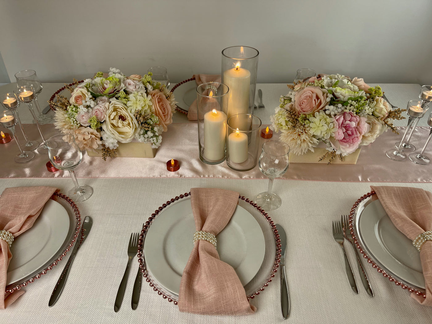 Clear plastic charger with rose gold beaded detail on edges featured in a table scape  with white tablecloth flowers and candles.