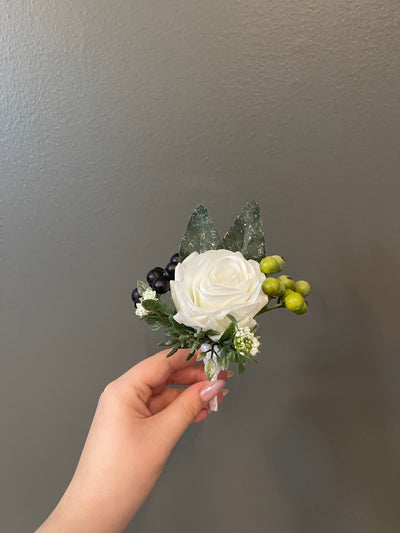 This 6" boutonniere features a white rose, green and black hypericum berries, and frosted eucalyptus. It is finished in a white satin ribbon.