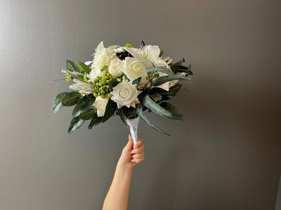 At the centre of this arrangement sits a single white peony surrounded by cream and white roses, white heaven lilies, cream ranunculus, white dahlia, white lavender, green and black hypericum berries. This enchanting sea of cream and white elegance is enveloped by frosted deep green eucalyptus. 