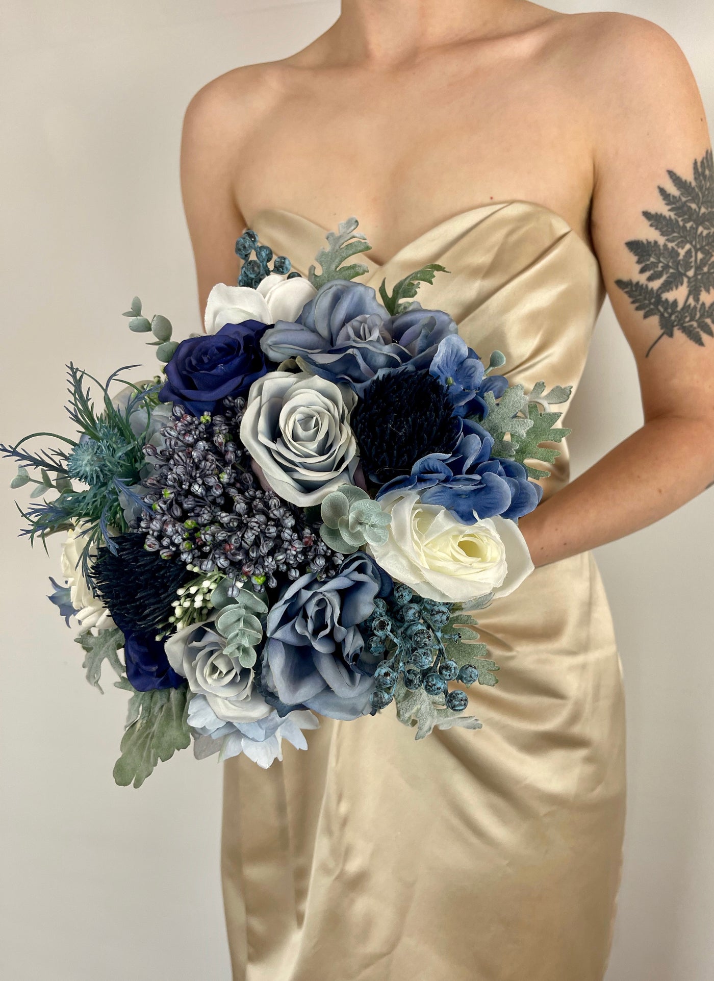 Blue bridesmaid bouquet being held by woman in champaign  coloured dress.