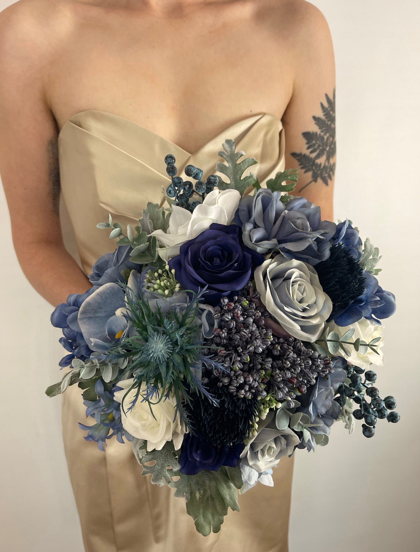 Blue bridesmaid bouquet being held by woman in champaign  coloured dress.