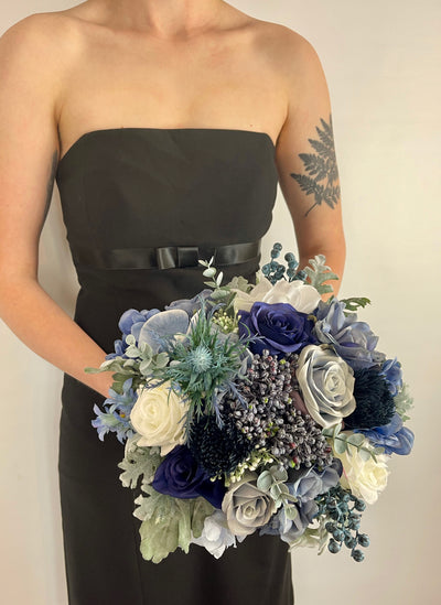 Blue bridesmaid bouquet being held by woman in black dress.