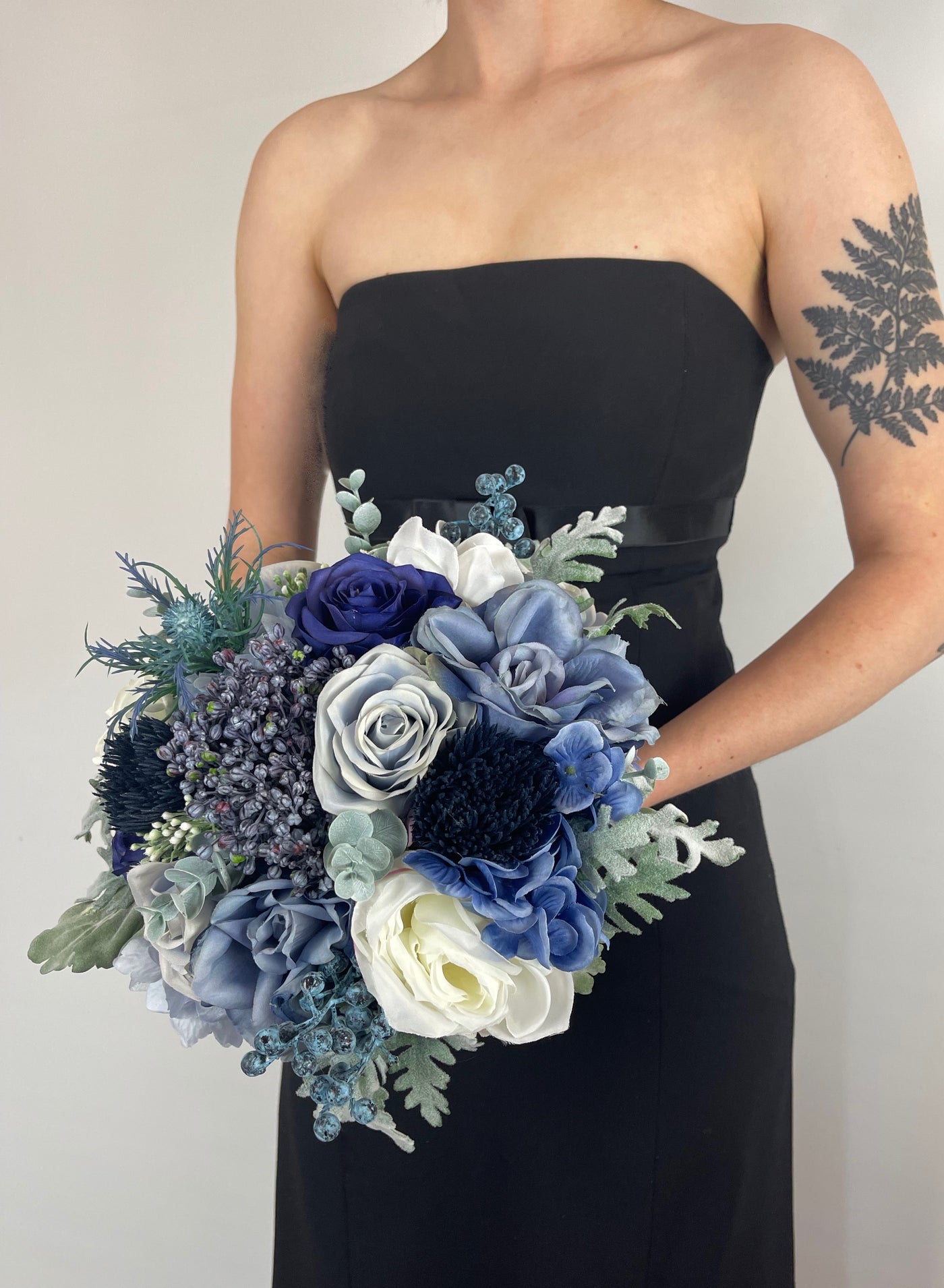 Blue bridesmaid bouquet being held by woman in black dress.