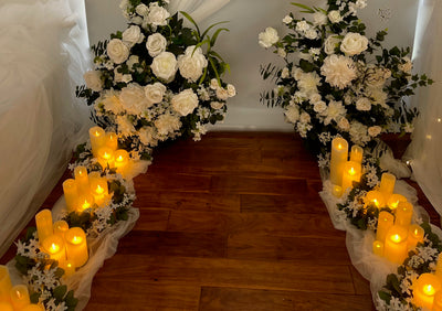 Two 4 feet x 3 feet round white floral arrangements shown at the end of a wedding aisle. The aisle is decorated with white mesh, white and dark green garland and various sizes of LED candles 