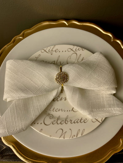 Delicate gold napkin ring holder, shown holding a white linen napkin folded like a bow on white and gold plates and an ornate gold charger. Rent for $.25