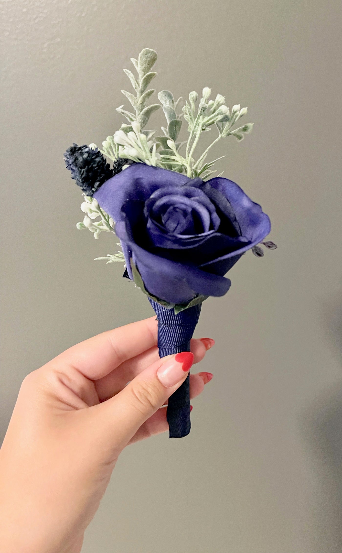 RentA Rose-boutonniere combines a single navy rose with two succulent spring of buttons sprigs and some dried navy thistle, neatly wrapped in a navy ribbon.
